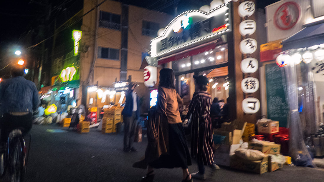 Two young girls walking in illuminated Asakusa (Japan) by night, with the city slightly blurred in the background.